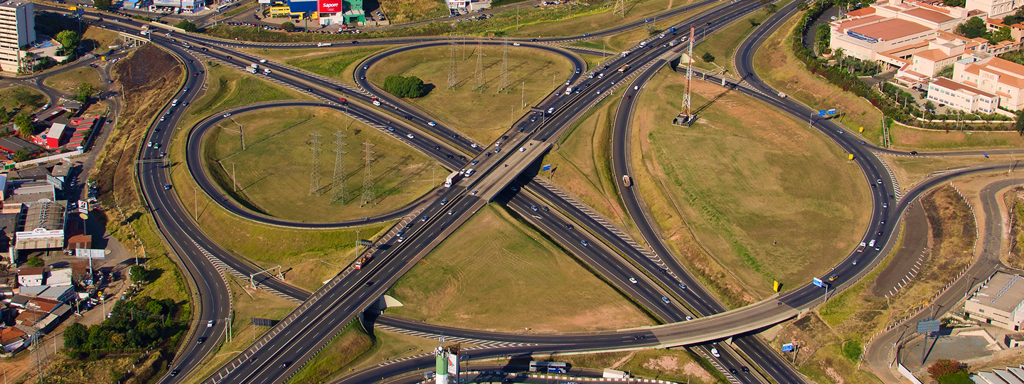 Vista aérea de um cruzamento de rodovias, mostrando várias faixas de tráfego e veículos em movimento.