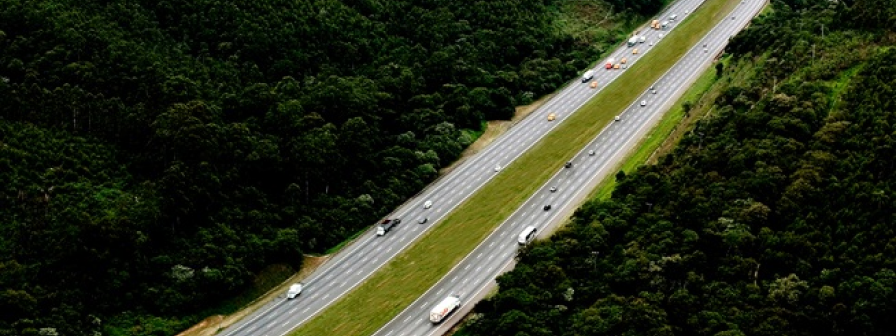 Vista aérea de rodovia duplicada cercada por área verde, com veículos em circulação em ambos os sentidos