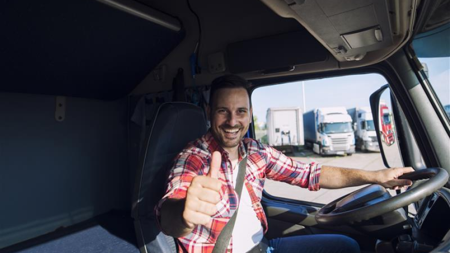 Caminhoneiro com uma mão no volante, fazendo um gesto de 'joinha' com a outra e sorrindo.