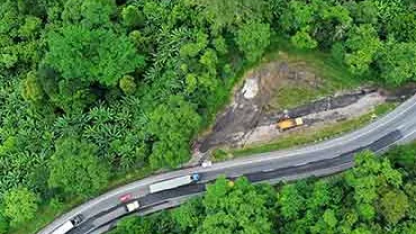Vista aérea de rodovia Serra das Araras sinuosa cortando área de mata densa, com veículos circulando entre o verde da floresta.