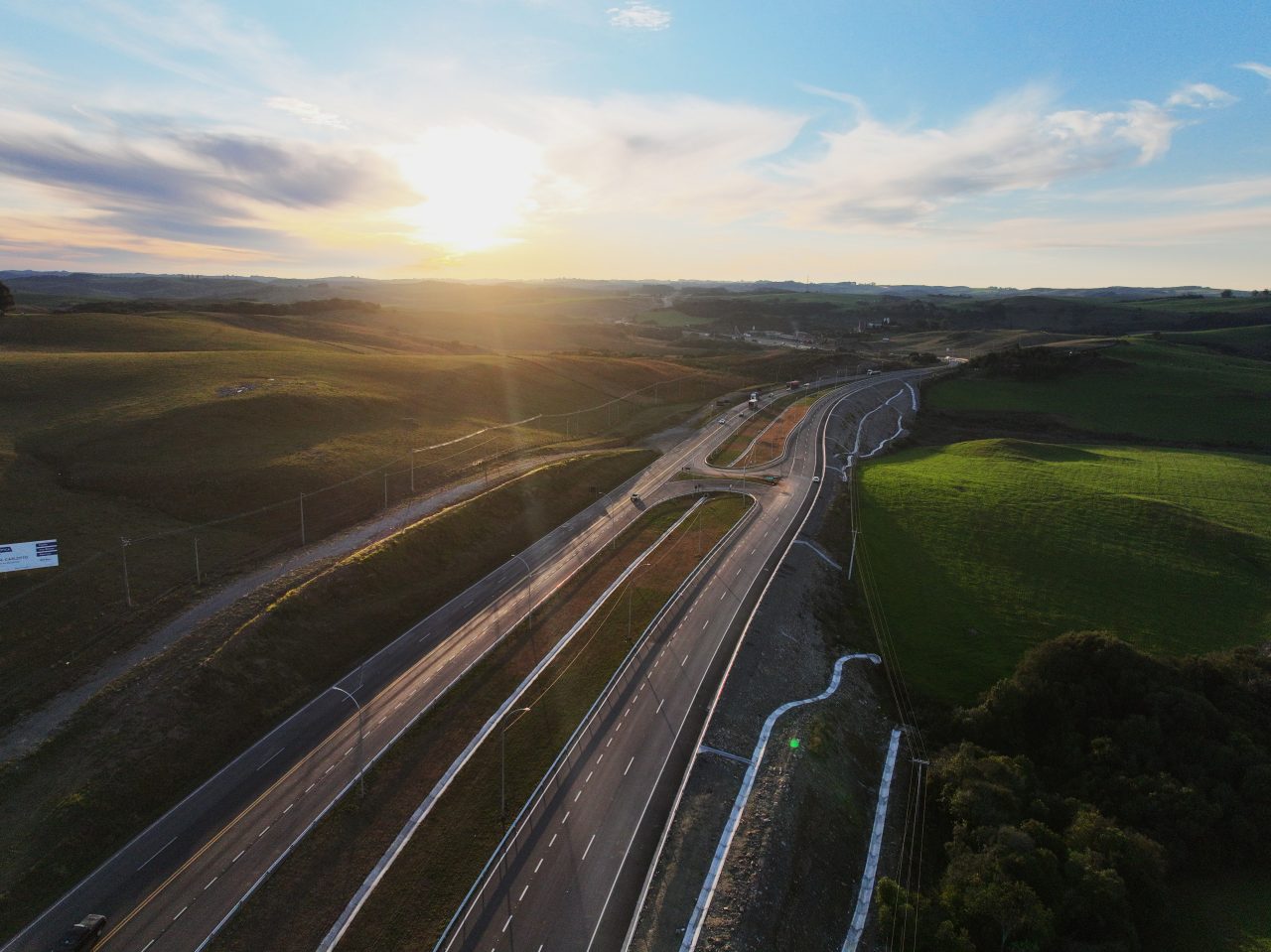 Vista aérea de uma rodovia com múltiplas faixas de tráfego próximas a edifícios, e plantações.