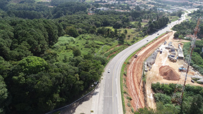 Vista aérea de rodovia em curva ao lado de área verde e trecho em obras de infraestrutura viária