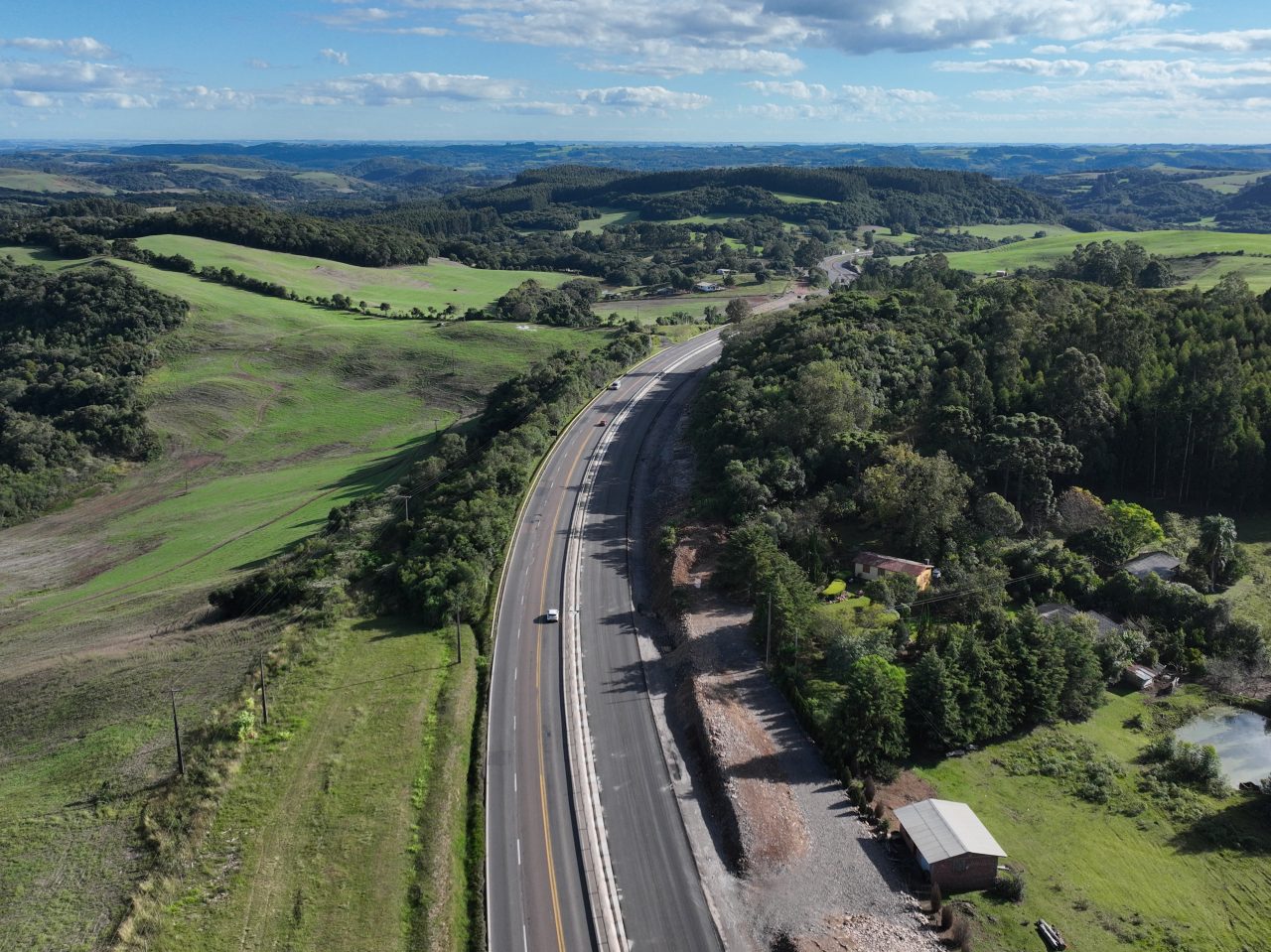 Perspectiva aérea de uma rodovia, com obras na marginal e maquinários trabalhando.