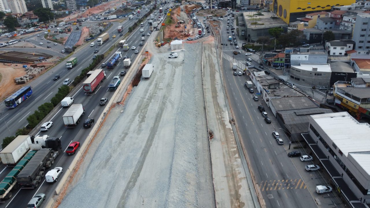 Imagem aérea mostra rodovia em Barueri entre galpões industriais e morro arborizado.