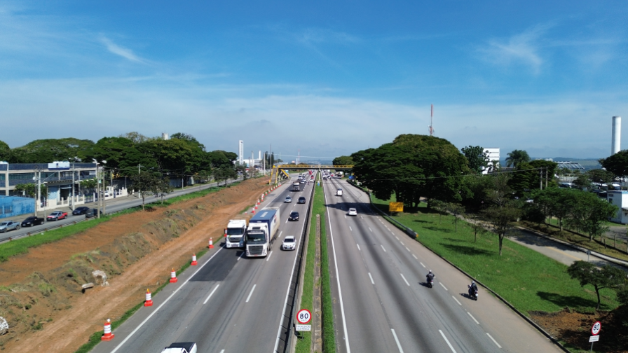 A imagem mostra um trecho da Rodovia Via Dutra com fluxo de veículos, incluindo carros e caminhões