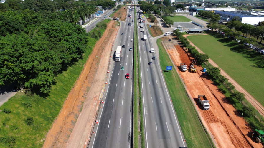 A imagem mostra a rodovia duplicada, com veículos em trânsito e obras de infraestrutura nas marginais