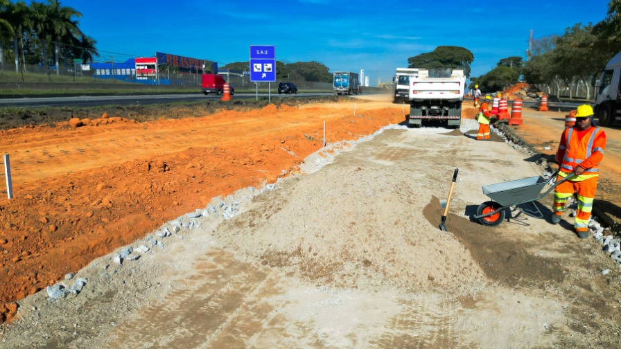 Trabalhadores realizam obras de novas pistas marginais, com terraplenagem e preparo do solo ao lado da rodovia.