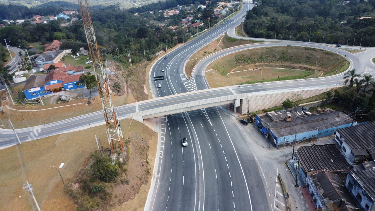 Vista aérea de um complexo viário em construção, mostrando novas faixas de rodovia, um viaduto e áreas residenciais ao redor.