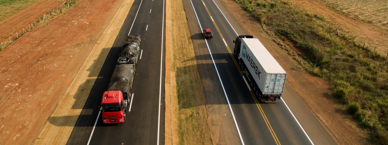 Rodovia de mão dupla da CCR MSVia, com um caminhão transitando à esquerda e um caminhão e um carro transitando à direita.