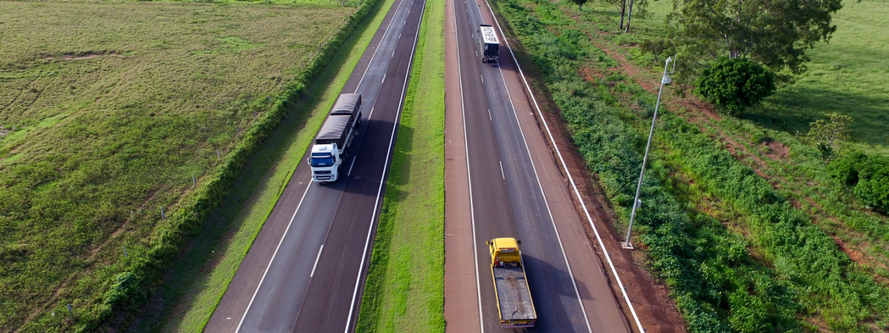 Rodovia de mão dupla da CCR MSVia, com um caminhão transitando à esquerda e um caminhão e um carro transitando à direita.