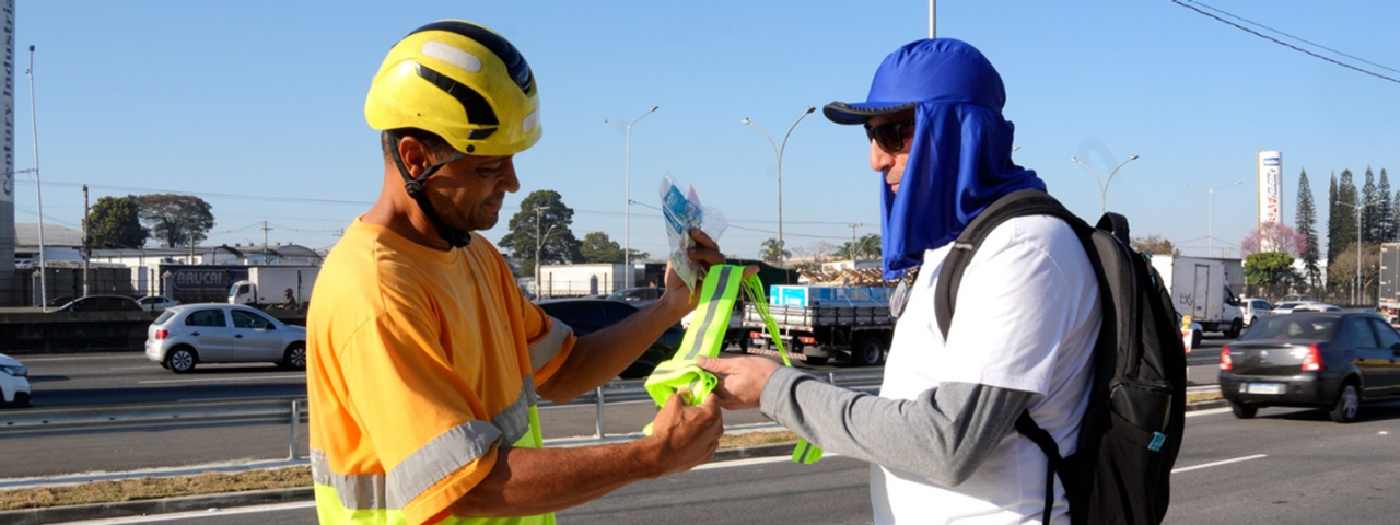 Homem entregando faixa de segurança para peregrino as margens da rodovia.