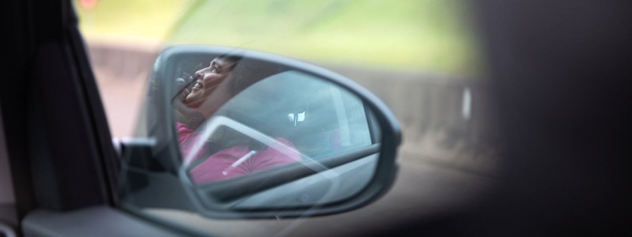 Retrovisor de carro refletindo uma mulher sorrindo.
