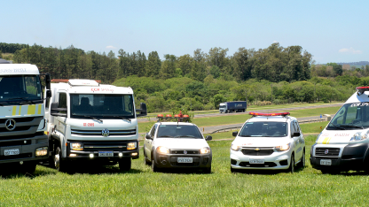 Veículos da CCR SPVias (guincho, caminhão-pipa, inspeção de tráfego, resgate e ambulância) em área com floresta e vegetação