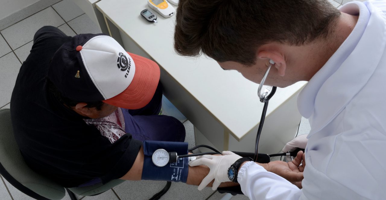 Médico aferindo a pressão arterial de um paciente, motorista de caminhão.