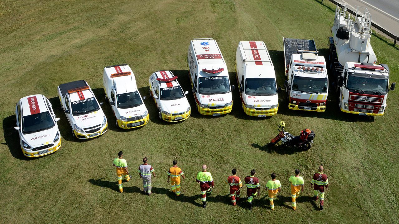 Um grupo de pessoas em pé em uma linha, ao lado de várias ambulâncias estacionadas.