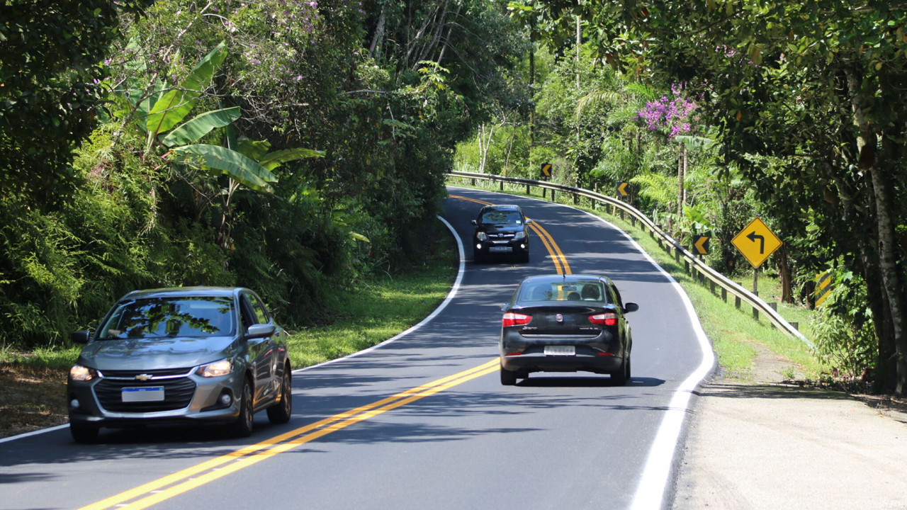 Carros em movimento na estrada, com um sinal de trânsito ao fundo.