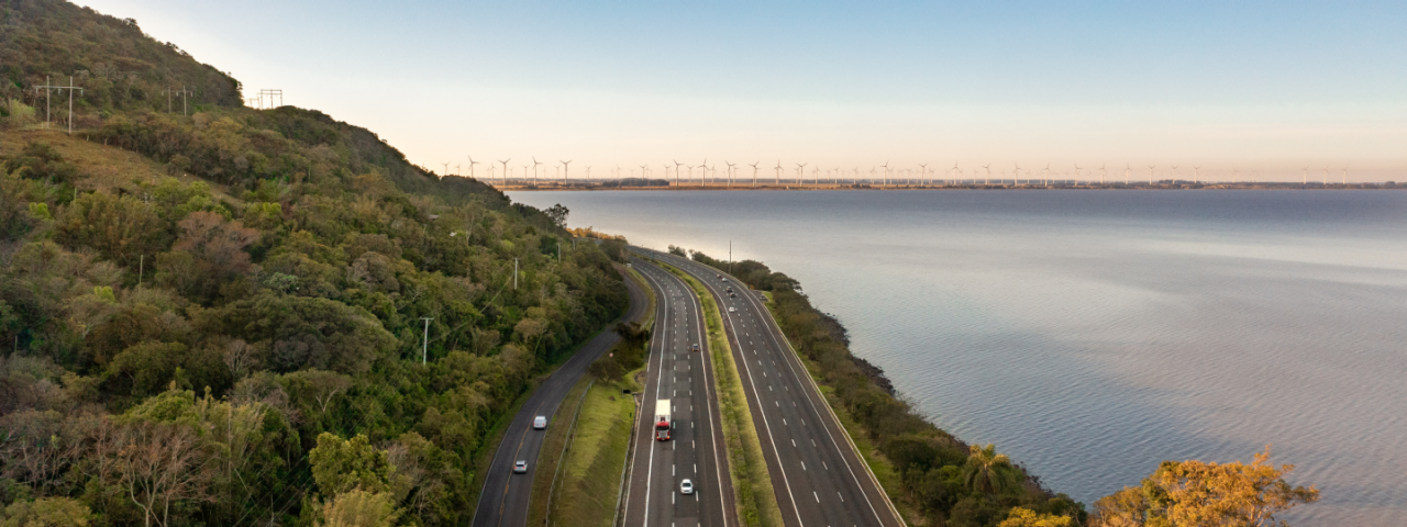 Rodovia administrada pela CCR Via Sul, com vista litorânea e parque eólico ao fundo